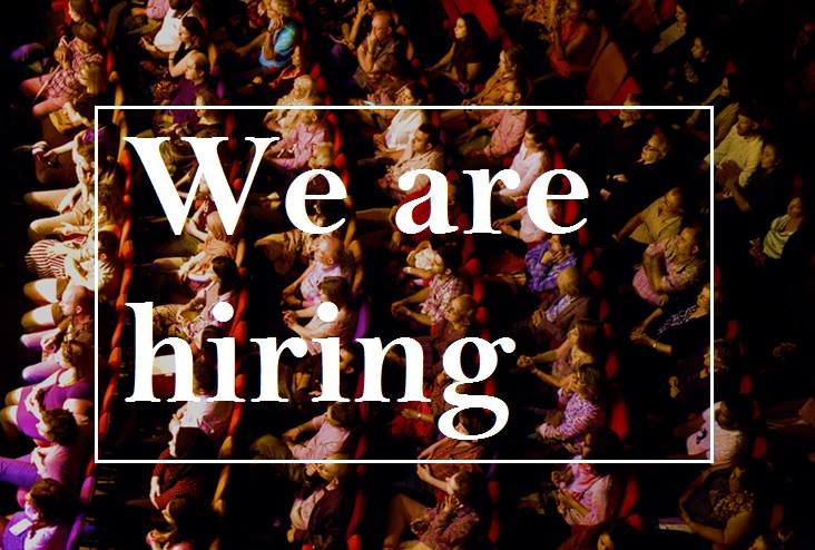 A photograph of an audience in an auditorium with a white box over the image with the words We Are Hiring in it.