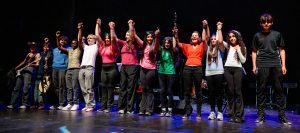 12 diverse young people on stage taking a curtain call at a Community Arts North West event.